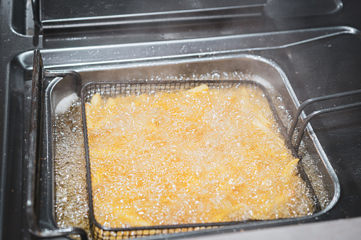 Frying French fries in cooking oil in a deep-fryer in kitchen