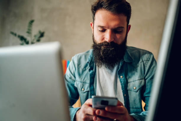 A digital marketer is sitting at his home office and typing on his cellphone, working on social media.