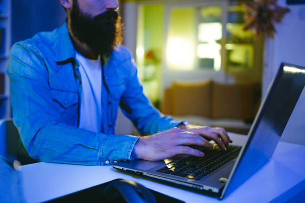 istock Hands of an AI developer typing on a laptop in his neon blue lighted home office. 1491063231