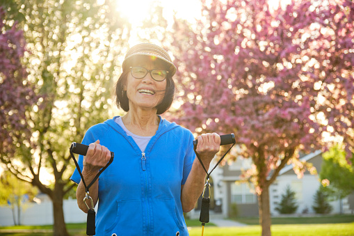A senior aged woman, exercising outdoors in a park.