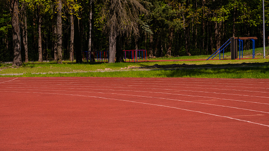 A running track in an empty stadium on a summer sunny day. Red rubberized track for running at the stadium in the park. The concept of competition in running..