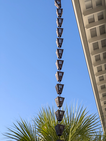 Rain chain, a series of decorative metal cups, hanging from the rooftop gutter of a building in a beach town in the Florida Panhandle