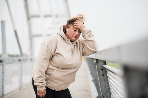 Portrait of an obese Latin woman resting after weight loss training. Obese woman catching her breath after jogging. Weight loss motivation. Fat woman struggling with weight. Body positivity. Plus size woman exercising. Weight loss journey.