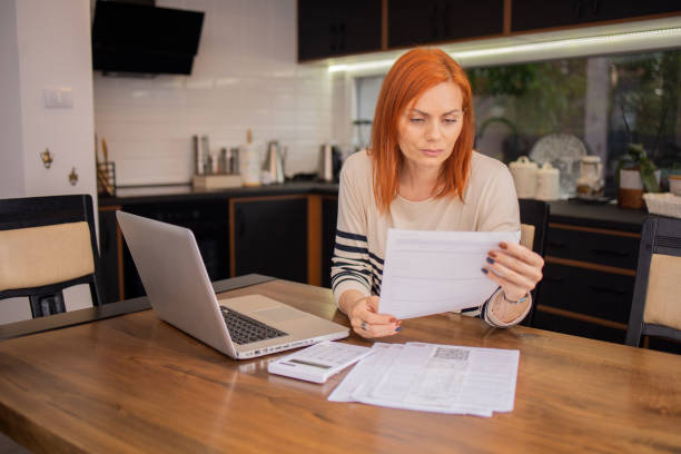 istock Mature woman using calculator while going through bills and home finances 1491084896