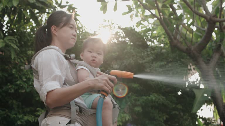 A mother holds her 7-month-old baby using a water nozzle for watering the plants