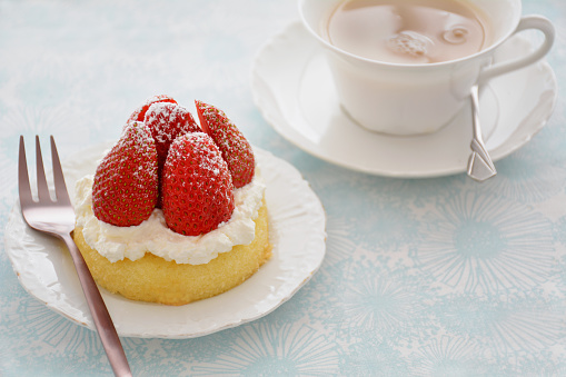 Fresh sweet strawberries with whipped cream on yellow sponge dessert cup and cup of tea in horizontal format.