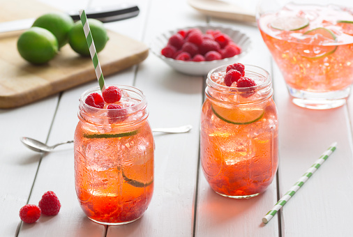 Raspberry lime iced tea in two glasses with straws. Ingredients for making tea are on the table in the background.