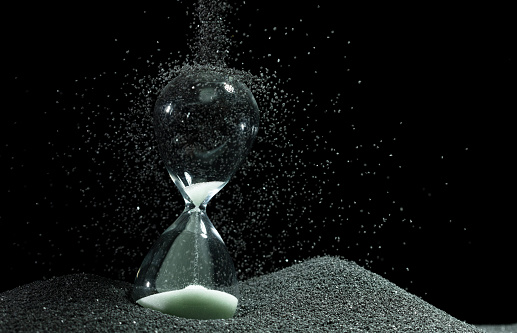 Hourglass stand on black sand with silhouette shadow over black background. Black hourglass show more time Deadline extended time management hope concept hour glass, life clock passing by