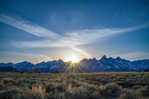 Grand Tetons wide view mountain scene and star burst with sun breaking behind peaks in the Yellowstone Ecosystem in western USA, North America. Nearest cities are Denver, Colorado, Salt Lake City, Moose, Moran, Jackson, Wyoming, Gardiner, Cooke City, Bozeman and Billings, Montana.
