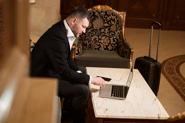 istock Man browsing something on portable notebook in armchair near baggage in hotel 1491121126