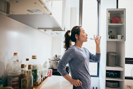 Young woman drinking a glass of water in kitchen at home