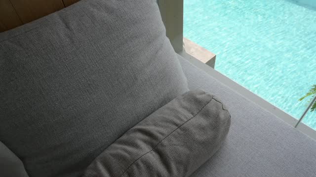 gray pillow put on bed, swimming pool view and slow motion water waves