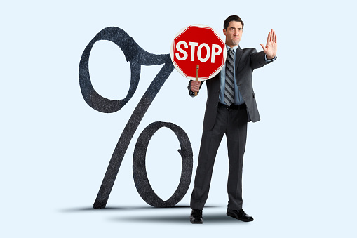 A businessman holds a stop sign as he stands in front of a large percentage sign.