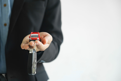 Close up hand of businessman, car dealer giving new car key to customer. Planning to manage transportation finance costs. Concept of car insurance business, saving buy â sale with tax and loan for new car.