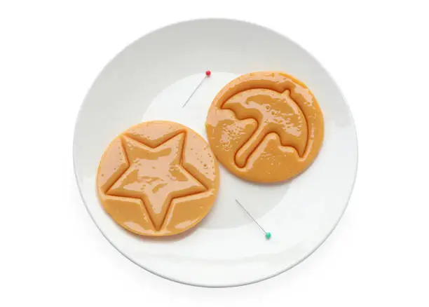 Photo of Dalgona candy or Ppopgi. Sugar Honeycomb cookie with round umbrella and star shape with needle on white plate. candy challenge, clipping path.