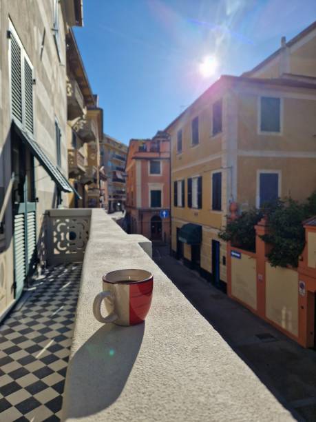 Espresso coffee cup throwing shadow on stone balcony in the morning on a quiet street in Liguria, Italy