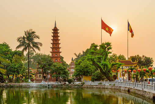 Hanoi, Vietnam - April 19, 2019: Awesome sunset view of the Tran Quoc Pagoda and West Lake. The flag of Vietnam (red flag with a gold star) and the Vietnamese Buddhist flag fluttering over the lake.