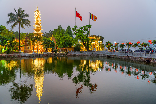 Hanoi, Vietnam - April 19, 2019: Fabulous evening view of the Tran Quoc Pagoda and West Lake. The flag of Vietnam (red flag with a gold star) and the Vietnamese Buddhist flag fluttering over the lake.