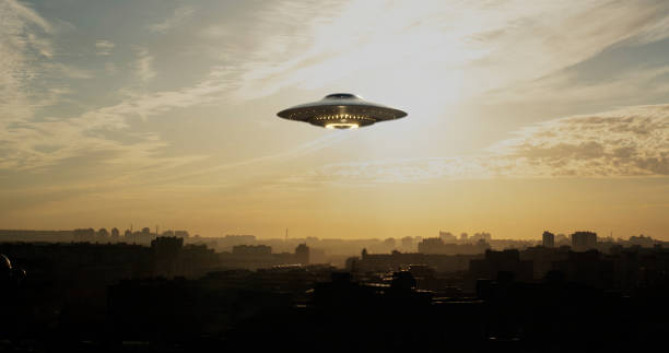 UFO saucer silently hovered over the city A strange flying machine in the shape of a saucer, silently hovering in the air. It emits a bright light and seems to scan the surrounding space with a beam. ufo stock pictures, royalty-free photos & images