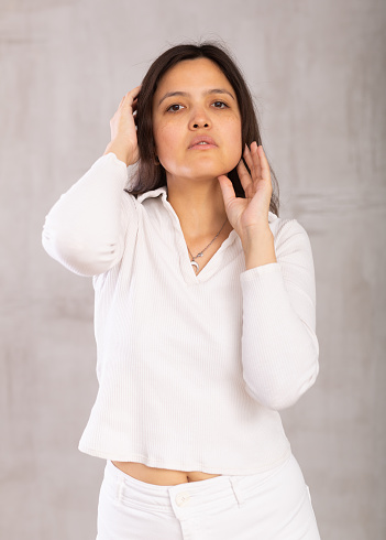 Portrait of an attractive young asian girl in a white trouser suit on a gray background