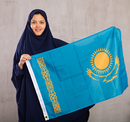 Closeup portrait of young positive woman in hijab posing in studio with flag of Kazakhstan