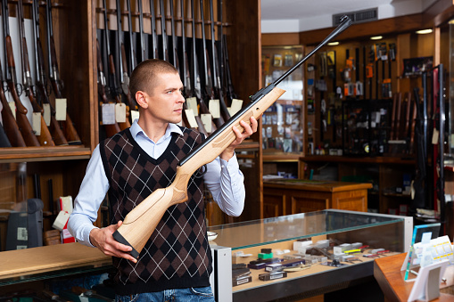 Portrait of man carefully choosing hunting break barrel rifle in modern gun shop