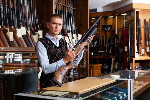 Gun shop salesman standing behind counter and showing modern sporting air PCP pump action rifle