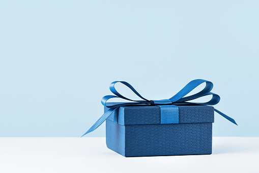 small Luxury gift box with a blue bow on light blue. Side view monochrome . Fathers day or Valentines day gift for him. Corporate gift concept or birthday party. Festive sale copy space