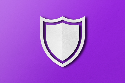 white paper shield Paper cut out punched shield shape set on purple paper background.