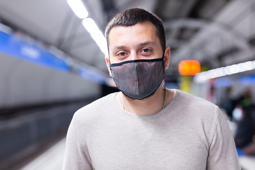 Young man in protective face mask walking through underground station, waiting for train. Necessary precautions during coronavirus pandemic