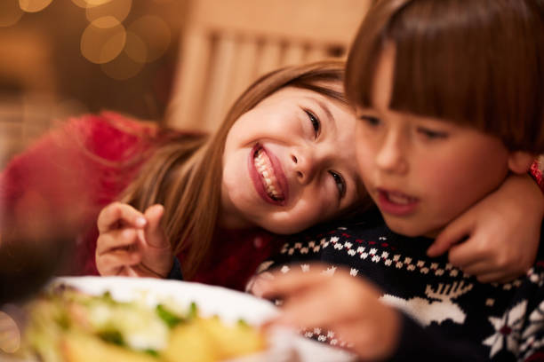 Close up of cute little girl embracing her brother during a meal at dining table.