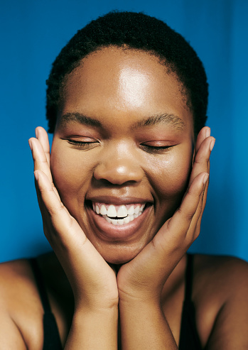 Portrait of a beautiful young black woman smiling with her hands covering her sides of her cheeks with her eyes closed. Stock photo