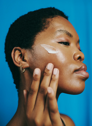 Beautiful headshot of a young black woman, looking down and thinking  as she applies moisturizer to her face with her head tilted backwards, stock photo
