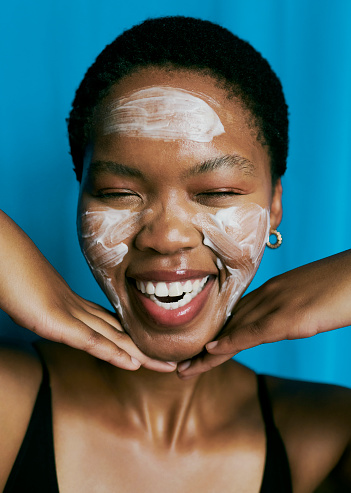 Front view of a beautiful black woman laughing with her eyes closed as she has applied facial mask as she shows off her beautiful smile stock photo