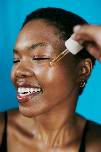 Face serum being applied to a beautiful black young woman with closed eyes as she enjoys a pampering session before getting in bed.  Image for beauty, skincare and self care. Stock photo.