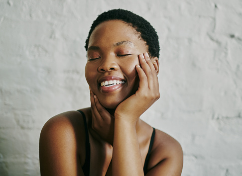 Shot of a beautiful young black woman smiling with her hands covering her sides of her cheeks whilst her eyes are closed. Image for beauty skincare and makeup. Stock photo