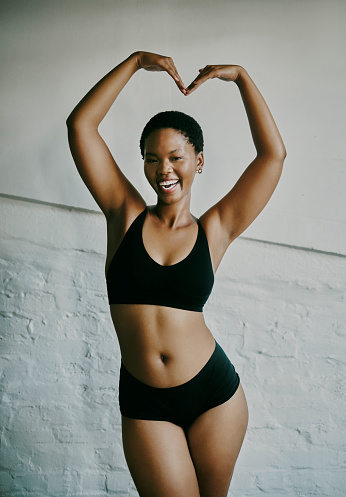 Photo of a young, attractive black woman standing and laughing while making the shape of a heart above her head