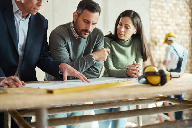 istock Young couple and their agent examining blueprints at construction site. 1491179809