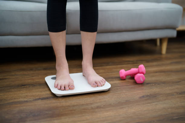 istock Fat diet and scale feet standing on electronic scales for weight control. Measurement instrument in kilogram for a diet control 1491180162