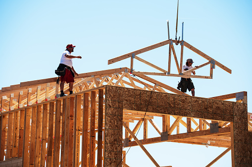 Framing Carpenters Reaching To Set a Roof Truss Being Lowered on to the Top of a Wall of a Home Being Built on a Sunny Day