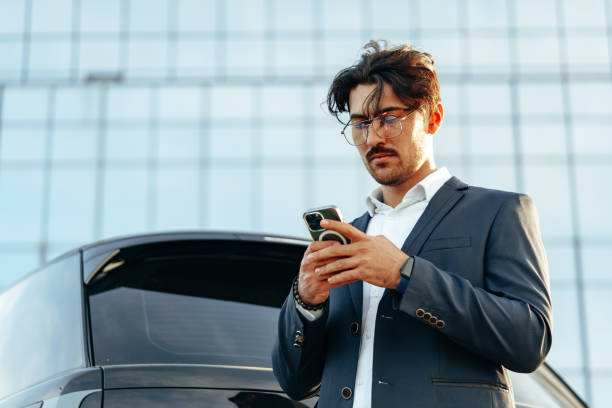 istock Young businessman standing near luxury car and using smartphone 1491180653