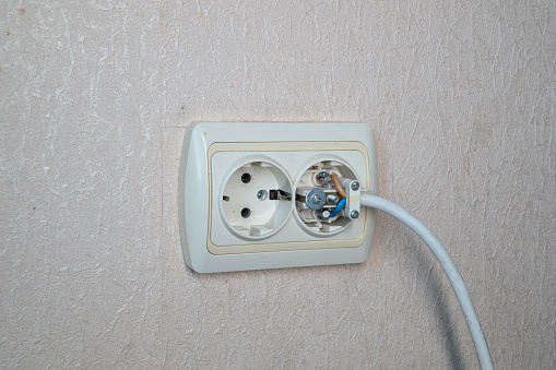 Household electrical outlet with a broken electrical plug inside. Bare live wires sticking out of the Electric socket installed in the wall and connected to the electricity power grid. Wiring Devices