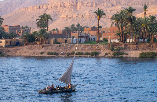 Nile Valley, Egypt - April 25, 2023: Felucca sailing past a village on the Nile River