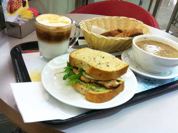Hands of a man in a suit with a glass of takeaway coffee and a triangular sandwich with tuna. Outdoor lunch and junk food concept.