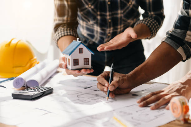 istock Professional architect, engineer or interior reviewing blueprint on workplace desk behind house model in office center 1491191444