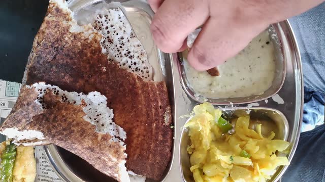 Closeup of a man eating masala dosa with mashed potatoes and coconut chutney