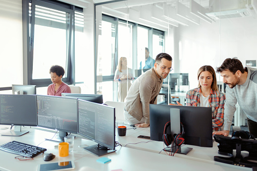 Startup business and entrepreneurship problem solving. Young AI programmers and IT software developers team brainstorming and programming on desktop computer in startup company share office space