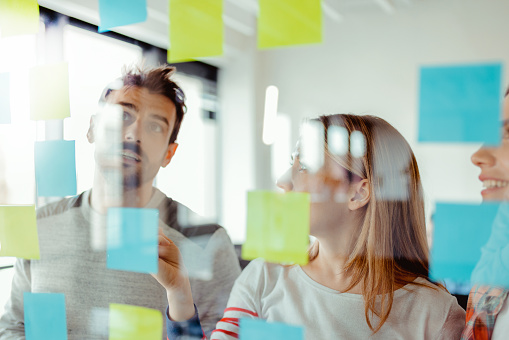 Business team looking at sticky notes on glass window in office