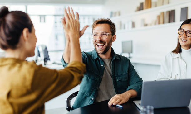 Business people celebrating success in an office Successful business people giving each other a high five in a meeting. Two young business professionals celebrating teamwork in an office. high five stock pictures, royalty-free photos & images