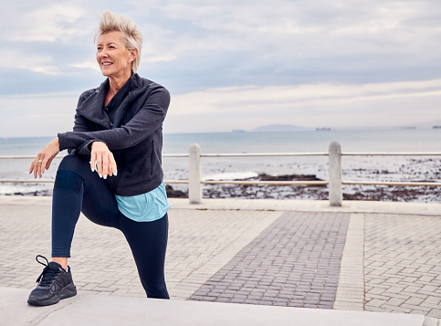 Senior woman, fitness and stretching at beach sidewalk for energy, wellness and happy workout on sky mockup. Elderly female, exercise and rest at sea promenade for training, sports run and motivation